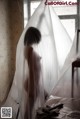 A naked woman standing in front of a bed covered in plastic.