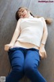 A woman in a white top and blue jeans laying on the floor.