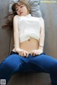 A woman laying on a wooden floor wearing a white top and blue jeans.