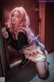 A woman with pink hair and glasses leaning against a door.