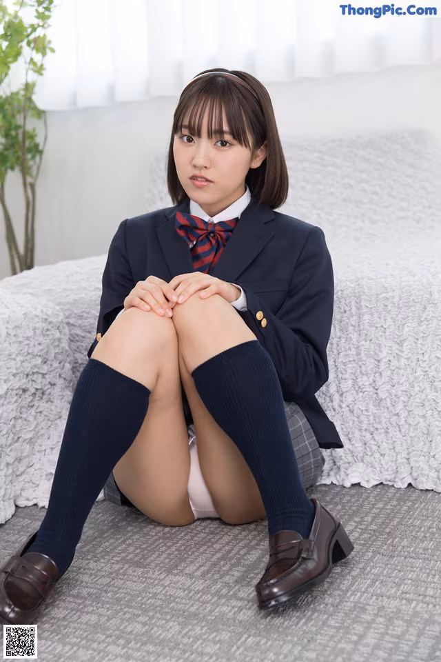 A young woman in a school uniform sitting on a couch.