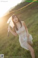 A woman in a white dress holding an umbrella in a field.