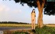 A naked woman wearing a face mask standing next to a tree.