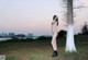 A naked woman standing next to a tree in a field.