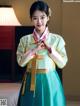 A woman in a green and yellow hanbok is posing for a picture.