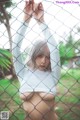 A woman in a white shirt is posing behind a fence.