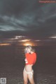 A woman in a red shirt and white bikini standing in the water.