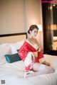 A woman in a red and white kimono sitting on a bed.