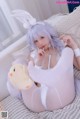 A woman in a white bunny costume sitting on a bed.