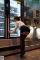 A woman standing in front of a refrigerator filled with bottles of alcohol.