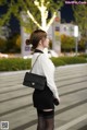 A woman in a white shirt and black skirt is walking down the street.