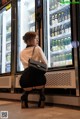 A woman in a white shirt and black skirt crouching in front of a refrigerator.