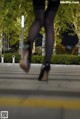 A woman in black stockings and high heels walking across a sidewalk.