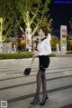 A woman in a white shirt and black skirt is walking down the street.