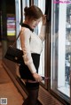 A woman in a white shirt and black skirt leaning against a refrigerator.