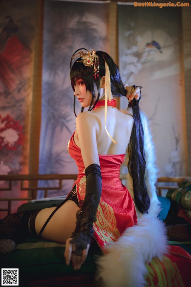 A woman in a red dress sitting on a bed.
