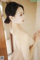 A naked woman leaning against a wall in a bathroom.