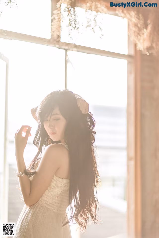 A woman in a white dress standing in front of a window.