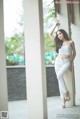 A woman leaning against a column in a white top and jeans.