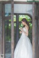 A woman in a wedding dress standing in front of a window.