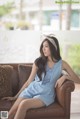 A woman sitting on a brown couch wearing a blue dress.