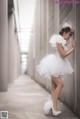 A woman in a white dress leaning against a wall.