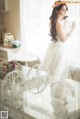 A woman in a wedding dress standing by a window.