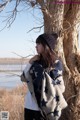 A woman leaning against a tree with a blanket around her neck.