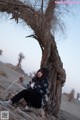 A woman sitting under a tree in the desert.