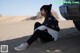 A woman sitting on the sand in front of a car.