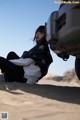 A woman sitting on the ground next to a car.