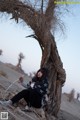 A woman sitting under a tree in the desert.