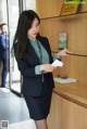 A woman in a business suit standing in front of a glass shelf.