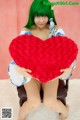 A woman with green hair holding a red heart.