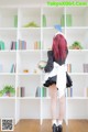 A woman in a maid outfit standing in front of a bookshelf.