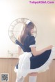 A woman in a maid outfit posing in front of a clock.