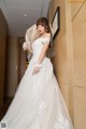 A woman in a wedding dress leaning against a wall.